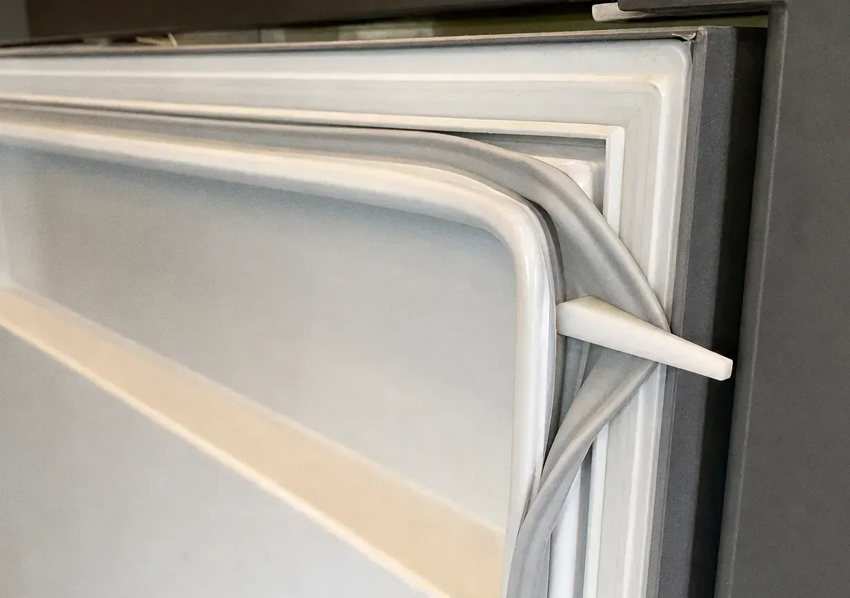 Close crop of a pale flexible door gasket running around the rounded corner of a refrigerator door