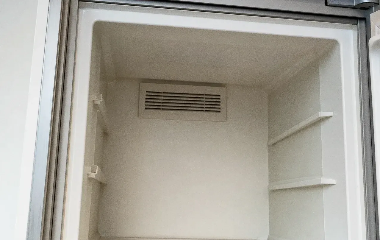 Empty white refrigerator cabinet interior with the rear air grille centred on the back wall